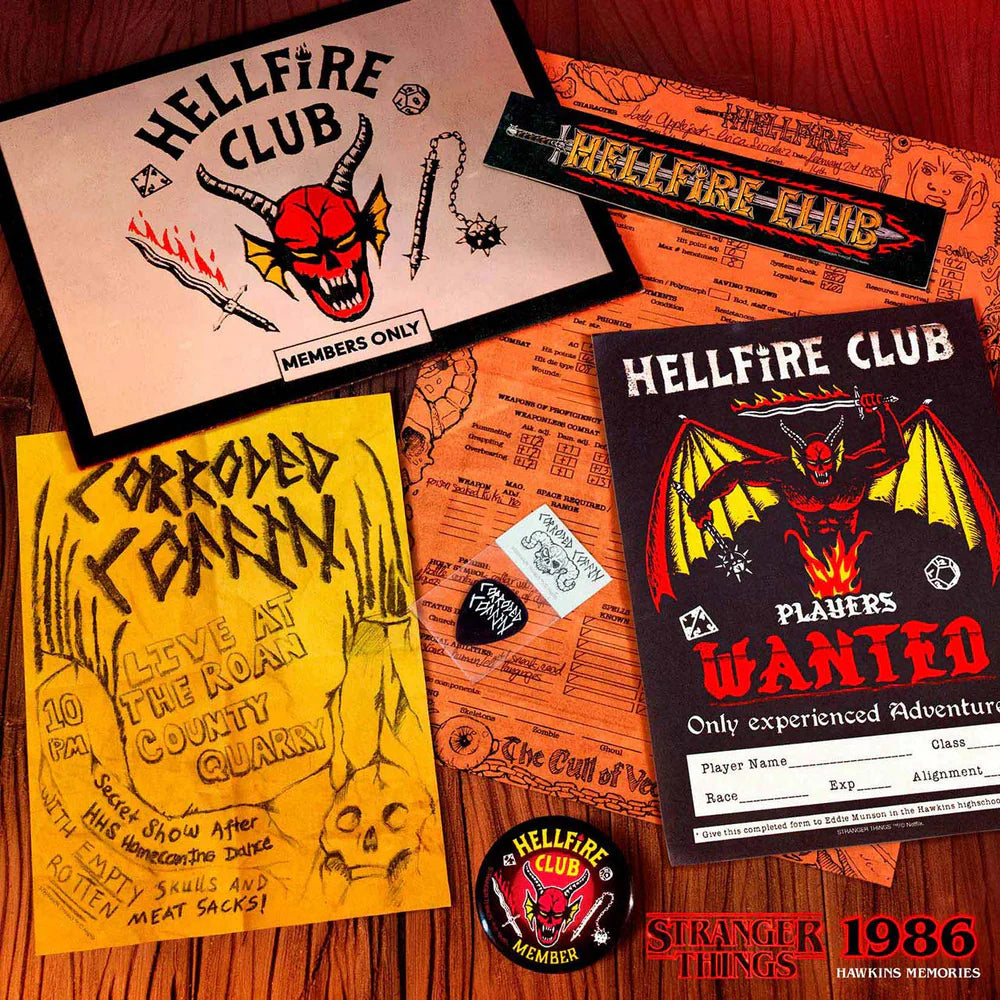 A flat lay of Hellfire Club themed memorabilia on a wooden surface, including a patch, a banner, a yellow 'Prohibited From Hell' sign, an orange map-style print, a black 'WANTED' poster, a pin, and a small sticker.